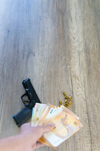 vertical photograph of hand with euro banknotes and pistol on a table and some blanks. copy space.