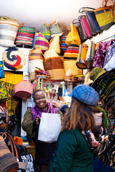 photograph of older black woman selling handicrafts in her store handing over the purchase with a smile on her face