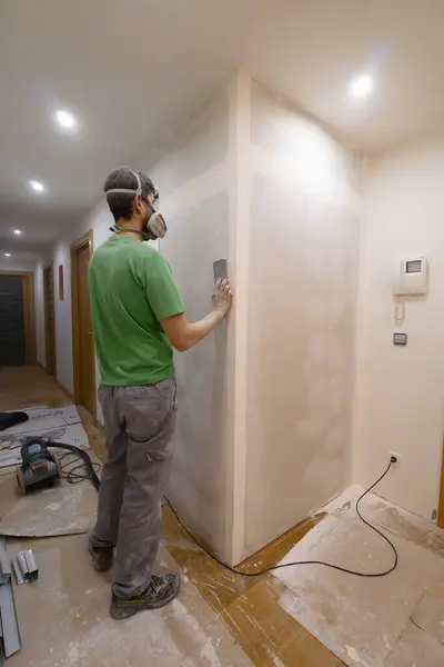 tired man works at home sanding drywall wall with a dust mask powdered housework