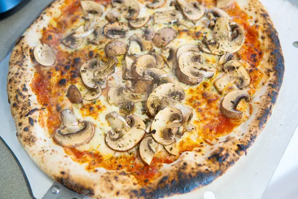 Photograph Chopped shot of a part of the pizza on an oven paddle. pizza, mushrooms, cheese, tomato, oregano. Homemade