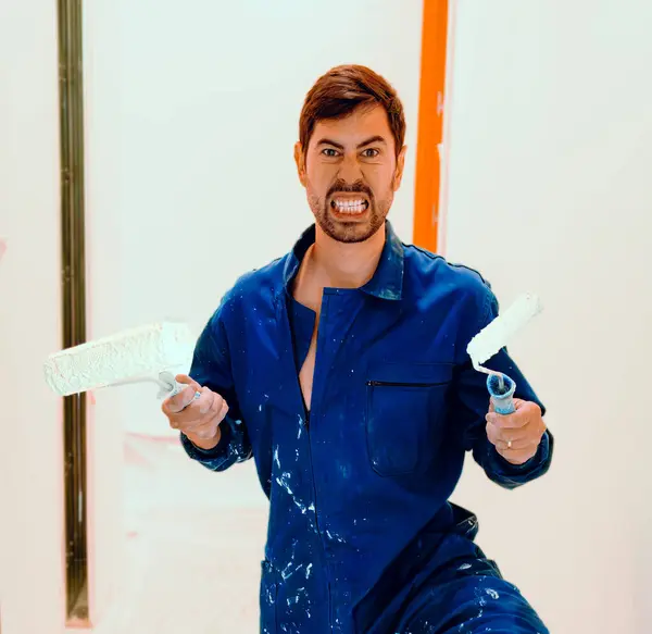 Humor at work. Funny man, crazy house painter with roller and brush. Crazy expression. He wears a worker\'s jumpsuit.