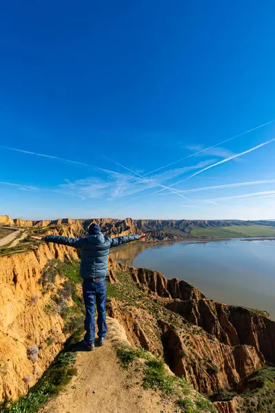 man with open arms on cliff top with lake below. arid land of canyons and gorges. Burujon Toledo Spain