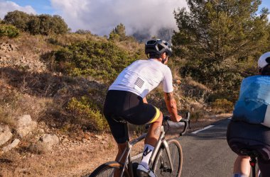 Gün batımında dağ yolunda bisiklet ve kask takan iki bisikletçi..