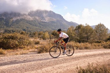 Çakıl yolu üzerinde pratik yapan bisikletçi. Taş yolda çakıl bisikleti süren formda erkek bisikletçi İspanya 'nın Alicante bölgesindeki dağları görüyor.