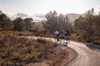 Bisikletli erkekler dağ manzaralı tepelerde, İspanya 'nın Alicante bölgesinde yolda çakıl bisikleti sürüyorlar..
