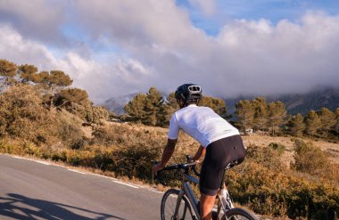 Boş dağ yolunda beyaz bisiklet forması ve kask eğitimi alan formalı formalı formalı bir bisikletçi. Rekabet için antrenman yapıyor. İspanya 'da spor amaçlı..