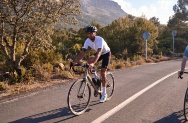 Boş dağ yolunda beyaz bisiklet forması ve kask eğitimi alan formalı formalı formalı bir bisikletçi. Rekabet için antrenman yapıyor. İspanya 'da spor amaçlı..