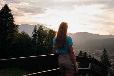 Gün batımında dağların önünde duran bir kadın yürüyüşçü. Resimli bir yerde gün batımı. Doğayla uyum kavramı.