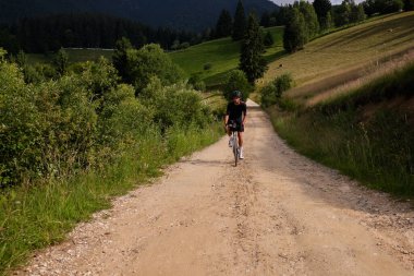 Çakıl yolunda pratik yapan profesyonel bisikletçi. Siyah bisiklet seti ve miğfer takan erkek bisikletçi. Dağlarda çakıllı yolda manzaralı bir manzarayla çakıl bisikleti süren adam..