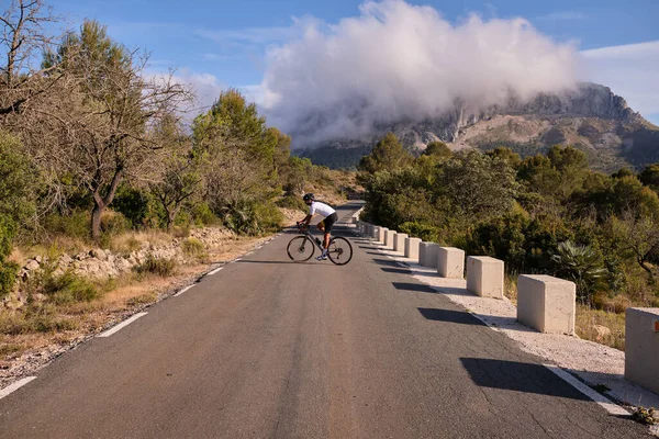 Male cyclist on a gravel bike is riding on the road in the hills with a view of the mountains.Sport motivation.Alicante region in Spain