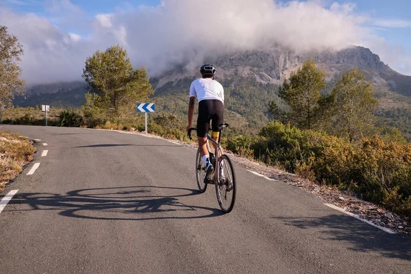 Male cyclist on a gravel bike is riding on the road in the hills with a view of the mountains.Sport motivation.Alicante region in Spain
