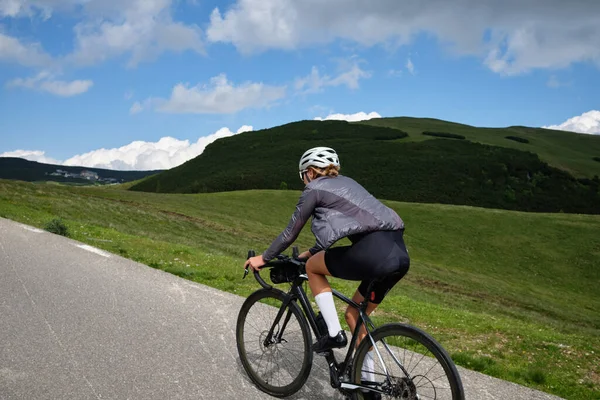 Woman cyclist riding a road bike with a view of the mountains. Sport motivation.Female cyclist wearing a cycling kit and helmet.Bucegi Mountains