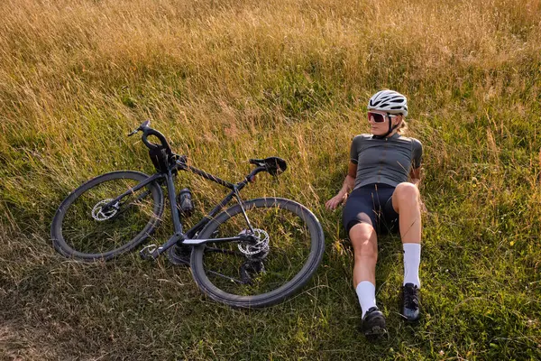 Woman cyclist wearing cycling green jersey, black shorts and helmet resting during training on the bicycle in the mountains.Road cycling concept.Woman cycling at sunset.