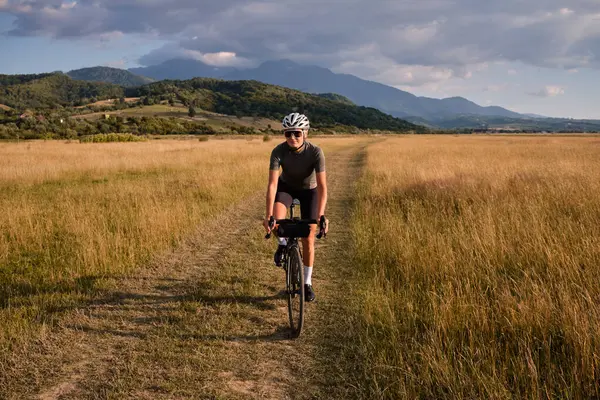 Fit female cyclist wearing cycling kit and helmet riding on the road on a gravel bike at sunset.Sports motivation image.