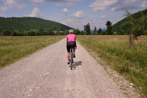 Female cyclist riding a gravel bike on a gravel road with a view of the mountains. Athlete is wearing cycling kit.