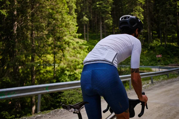 Gravel ride. Professional cyclist training hard in a beautiful forest. Man is cycling in the nature. Male cyclist wearing cycling kit and helmet.