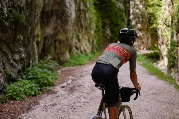 Male cyclist riding a gravel bike through rocky mountain terrain. Gravel biking adventure on beautiful mountain trails. Outdoor sport activity.