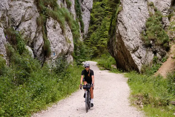 Female cyclist riding a gravel bike through rocky mountain terrain. Gravel biking adventure on beautiful mountain trails. Outdoor sport activity.Fit pretty cyclist training on nature.