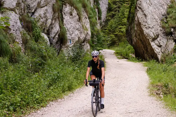 Female cyclist riding a gravel bike through rocky mountain terrain. Gravel biking adventure on beautiful mountain trails. Outdoor sport activity.Fit pretty cyclist training on nature.