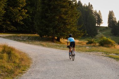 Mavi bisiklet forması giyen bir bisikletçi. Gün batımında çakıllı bir yolda dağ manzaralı çakıl bisikleti sürüyor. Roma 'da boş dağ yolu. Bucegi Doğal Parkı.