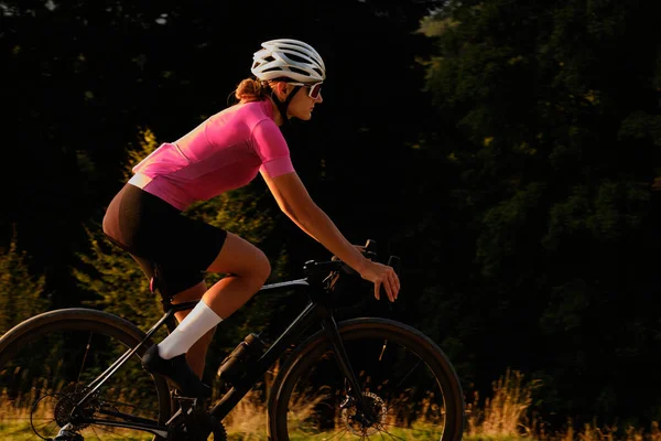 Закате Женщина Велосипедистка Розовой Велосипедной Майке Белом Шлеме Едет Велосипеде — стоковое фото