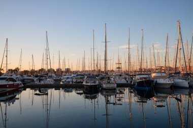 Gün batımında yat parkında. Günbatımında yatları olan deniz koyunda. Demirli yatlar. Marina, iskele. Gün batımında gemi direklerinin deniz suyuna yansıması. Torrevieja, Alicante, İspanya