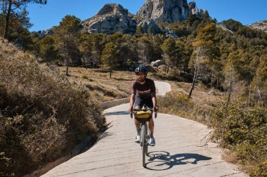Dağların manzarası ile tepelerde bisiklet süren bir bisikletçi. Bisiklet seti ve kask takan bisikletçi. Bisiklet çantalı çakıl bisikleti.