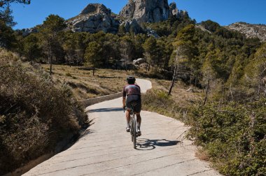Manzaralı dağlarda çakıllı yolda bisiklet süren bir adam. Çakıl bisiklet macerası. Bir atletin güzel motivasyon görüntüsü. Guadalest Reservoir, Alicante, İspanya.