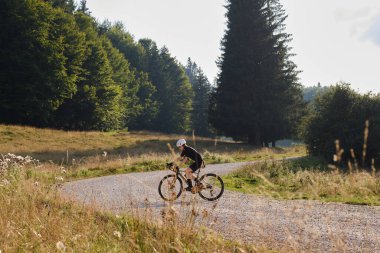 Siyah bisiklet seti giyen bir kadın bisikletçi. Gün batımında çakıllı bir yolda dağ manzaralı çakıl bisikleti sürüyor. Boş dağ yolu. Romanya 'da çakıl taşı macerası. Bucegi Doğal Parkı.