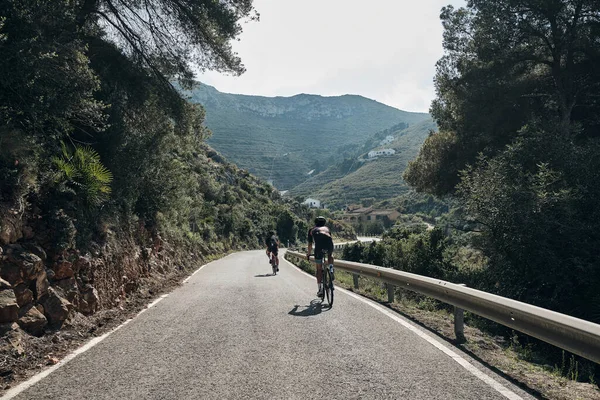 两个骑自行车的人在山路上训练 在西班牙山区骑自行车 骑自行车的人戴头盔和骑自行车 运动动机 骑自行车的专业团体 美丽的风景 西班牙阿利坎特 萨比亚 — 图库照片