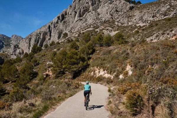 A female cyclist is training on a mountain pass on a gravel bike.Woman riding on bicycle in the mountains.Cyclist wearing a cycling kit and helmet.Gravel cycling adventure.Guadalest Reservoir,Spain.
