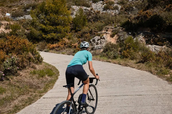 骑自行车的女骑手骑着自行车和头盔爬上山路的女骑手 骑自行车的女骑手骑在山间 塑造了一个美丽而有激情的运动员形象 — 图库照片