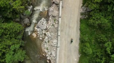 Üst görüntü drone görüntüsü. Yeşil formalı bir bisikletçi dağların arasında çakıllı bir yola çıkıyor. Çakıl bisikleti macerası..