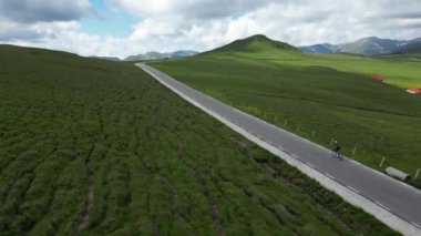 Dağlarda kadın bisikletçi eğitimine ait drone görüntüleri. Profesyonel kadın bisikletçi, manzaralı boş bir yolda gidiyor. Nefes kesici manzaralar ve yetenekli bir kadın bisikletçi..