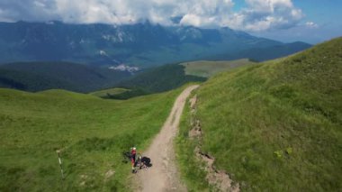 İki bisikletçi dışarıda, dağlarda bisikletlerini tamir ediyor. Enduro izleri. Bisiklet arkadaşlarının izini sürüyorum. İnsansız hava aracı dağ bisikletçilerini yokuş aşağı takip ediyor..