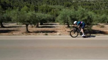 Ağır çekim video 4K.Bisiklet Tatili İspanya 'da. Profesyonel erkek bisikletçi, deneme sürüşü bisikletine biniyor. Aero bisiklet seti ve beyaz başlık takıyor. Triatlon antrenmanı..