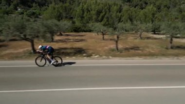Yol bisikletçisi yavaş çekim videosu. Boş yolda zaman bisikleti süren erkek bisikletçi. Aero bisiklet seti ve beyaz başlık takan bisikletçi..