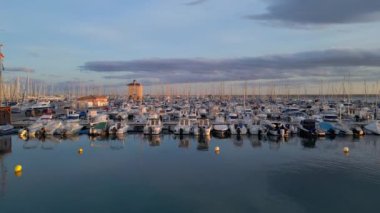 Grand Marina 'da kıyıda duran lüks tekne ve kayıklar. Günbatımı videosunda yatlarla marina üzerinde İHA uçuşu.