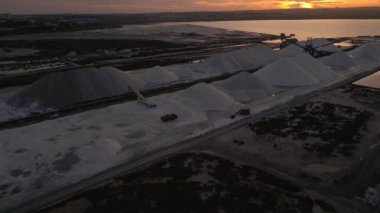 Güzel altın gün batımında altın gölün üzerinden beyaz tuz tepelerine doğru uçuyor. Hava aracı görüntüleri, ileri hareket. Fabrica del Sal, Torrevieja, İspanya