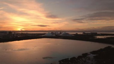 Güzel altın gün batımında altın gölün üzerinden beyaz tuz tepelerine doğru uçuyor. Hava aracı görüntüleri, ileri hareket. Fabrica del Sal, Torrevieja, İspanya