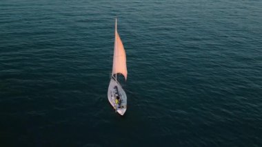 Pembe yelkenli beyaz yelkenli yat günbatımında turkuaz deniz dalgalarında yüzüyor. Hava aracı görüntüleri. Alicante, İspanya