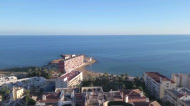Kamera renkli yüksek binalardan uzaklaşarak deniz kıyısı ve apartmanlı bloğu gösteriyor. Emlak satışı videosu. Torrevieja, İspanya