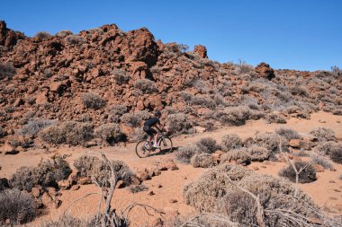 Çakıl yolunda çalışan bir bisikletçi. İspanya 'nın Tenerife Kanarya Adası' ndaki Teide volkanı manzaralı çakıllı yolda çakıl bisikleti süren formda bir bisikletçi. Bisikletli çakıl macerası. Efor havası.