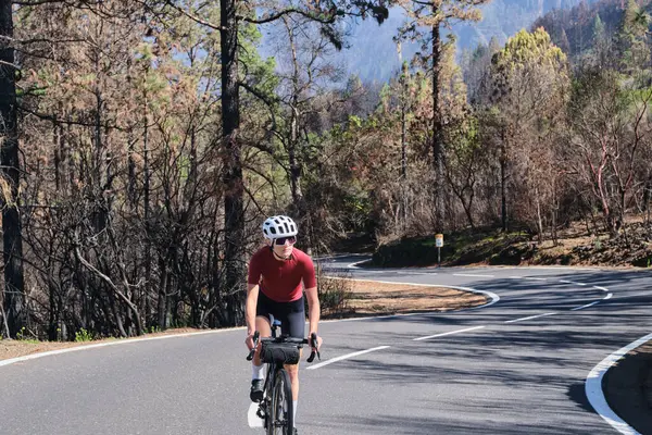 İspanya 'nın Kanarya Adaları, Tenerife' deki yanmış ormanda asfalt yolda bisiklet süren bir kadın. Spor motivasyonu. İspanya 'da bisiklet eğitimi. Bisiklet macerası. Güzel doğada pedal çevirmek..