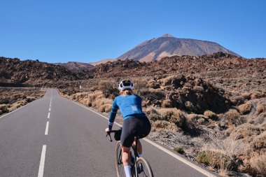 Tenerife, Kanarya Adaları, İspanya 'daki Teide Dağı volkanı manzaralı yolda pedal çeviren bir kadın. Spor motivasyonu. Dışarıda bisiklet eğitimi. Hippi bisikletçi..