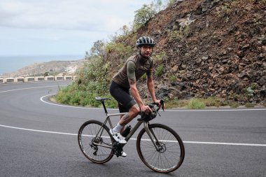 Bir erkek bisikletçi yolda bir bisiklet sürüyor. Yarışma için antrenman. Açık kırsal yolda bisiklet sürme pratiği. Tenerife, Kanarya Adası 'nda bisiklet macerası.
