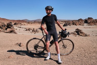 Çakıl yolunda çalışan bir bisikletçi. Çakıl yolundaki çakıllı bisikletinin yanında duran formda bisikletçi Tenerife, Kanarya Adası, İspanya 'daki Teide volkanı manzaralı. Çakıl taşı macerası..