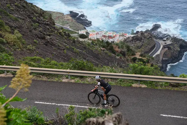Bisikletli bir kadının dağ ve okyanus manzaralı en iyi manzarası. Bisiklet macerası. Bisiklet çantası ve kask takan bir kadın bisikletçi. Tenerife, Kanarya Adası, İspanya. Virajlı yol.
