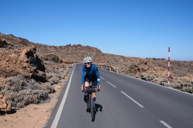 Arka planda bir volkan olan bisiklet süren bir kadın bisikletçi. Tenerife.Bisikletle yolculuk. Teide Dağı 'na giden yol. Bisiklet seti ve kask takan kadın bisikletçi. İspanya.