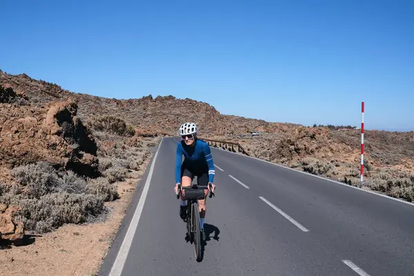 Arka planda bir volkan olan bisiklet süren bir kadın bisikletçi. Tenerife.Bisikletle yolculuk. Teide Dağı 'na giden yol. Bisiklet seti ve kask takan kadın bisikletçi. İspanya.